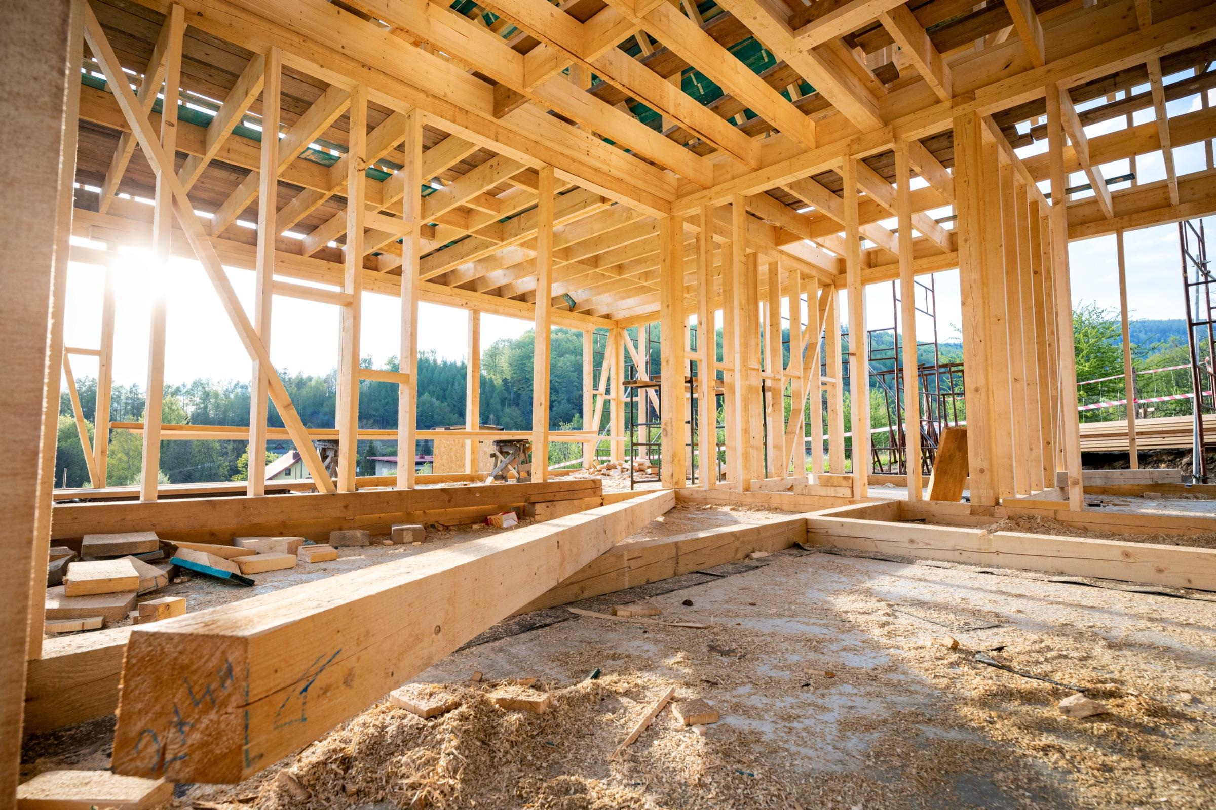Wood stud framing of a new home under construction, open walls and roof trusses in sunlight